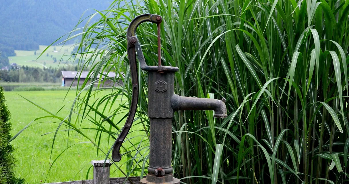 Bomba manual de poço em área rural com plantação ao fundo