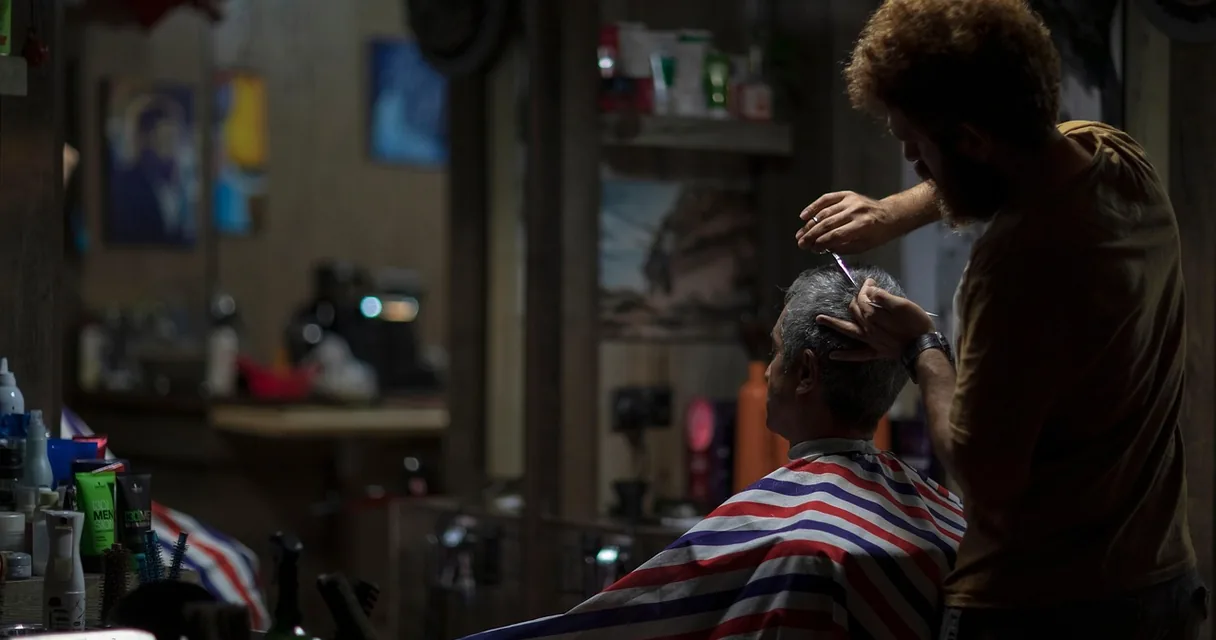 Barbeiro cortando o cabelo de um cliente em uma barbearia, ilustrando o IPTV na barbearia