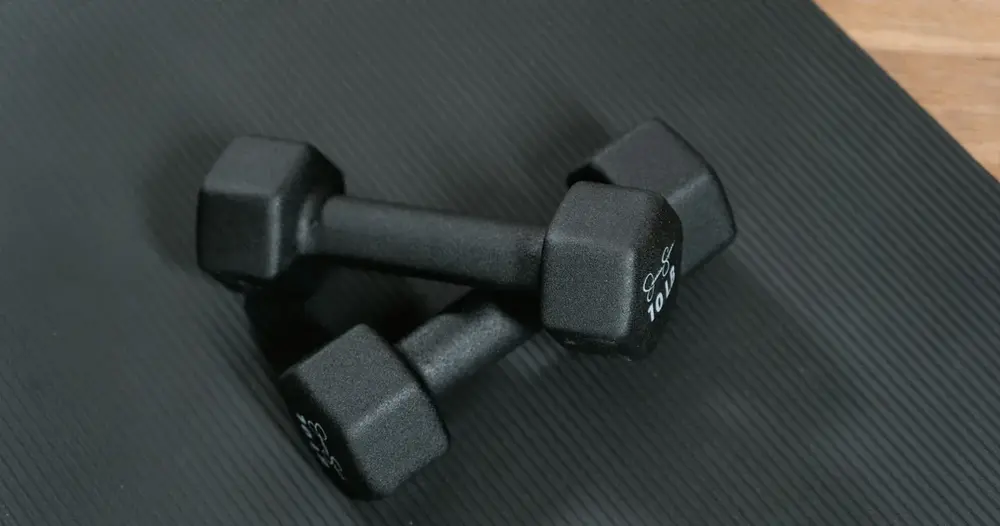 Dois halteres pretos sobre um tapete de treino, ilustrando os sites para saber quanto ganha um personal trainer