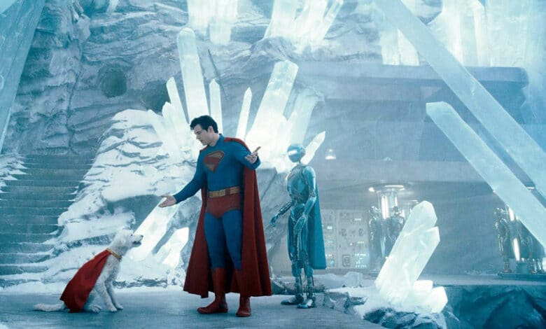 A imagem mostra um personagem vestido como super-herói, com um traje azul e uma capa vermelha, interagindo com um cachorro que também usa uma capa vermelha. Ao fundo, há uma estrutura de cristais de gelo e um robô prateado. O ambiente é gelado e iluminado, com uma atmosfera futurista.