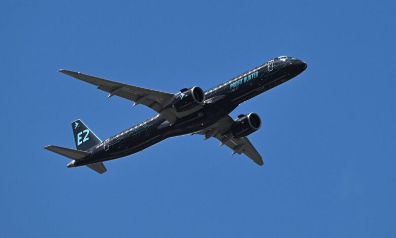 Um avião comercial está voando em um céu azul claro. O avião é de cor preta com detalhes em verde e possui a inscrição