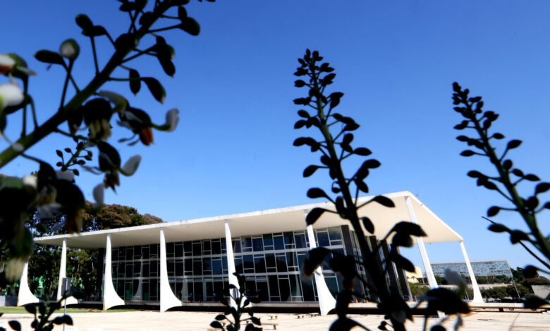 Em primeiro plano, silhueta de folhas em frente ao jardim do edifício sede do STF, que aparece ao fundo. Dia claro de céu azul.