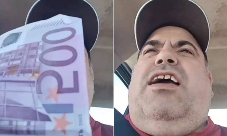 A imagem mostra um homem segurando uma nota de 500 euros em uma mão, enquanto fala para a câmera. Ele está usando um boné e uma camiseta vermelha. O fundo parece ser o interior de um veículo, com luz natural entrando pela janela.