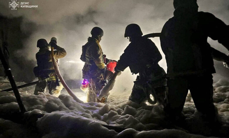 A imagem mostra bombeiros trabalhando em um ambiente com fumaça densa e espuma. Eles estão equipados com capacetes e roupas de proteção, utilizando mangueiras para combater um incêndio. A iluminação é baixa, criando um efeito dramático com sombras e luzes refletidas na espuma ao redor.