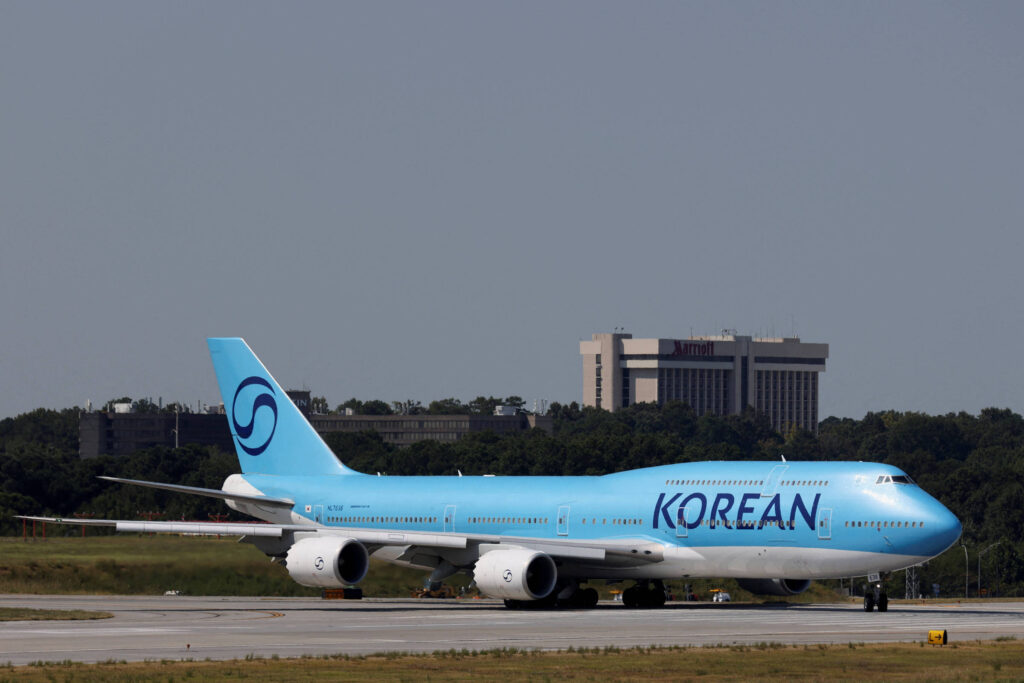 Um avião da Korean Air, modelo Boeing 747, está taxiando na pista de um aeroporto. A aeronave é predominantemente azul, com a palavra