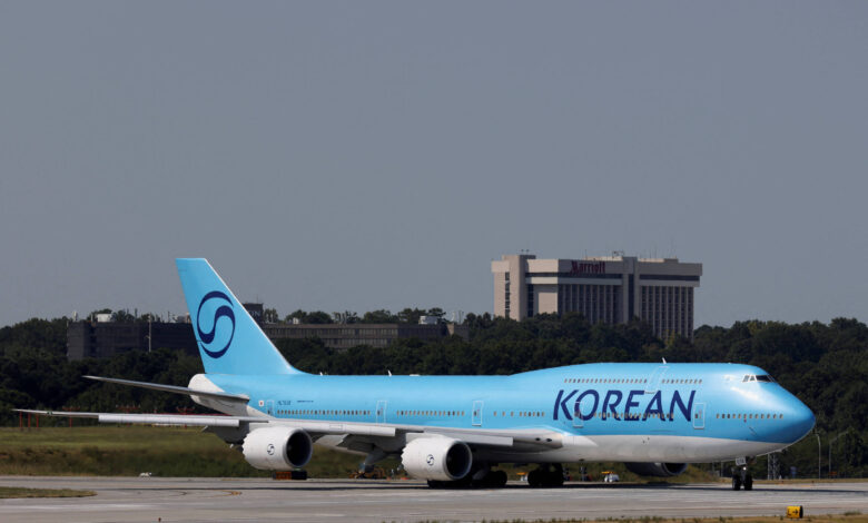 Um avião da Korean Air, modelo Boeing 747, está taxiando na pista de um aeroporto. A aeronave é predominantemente azul, com a palavra