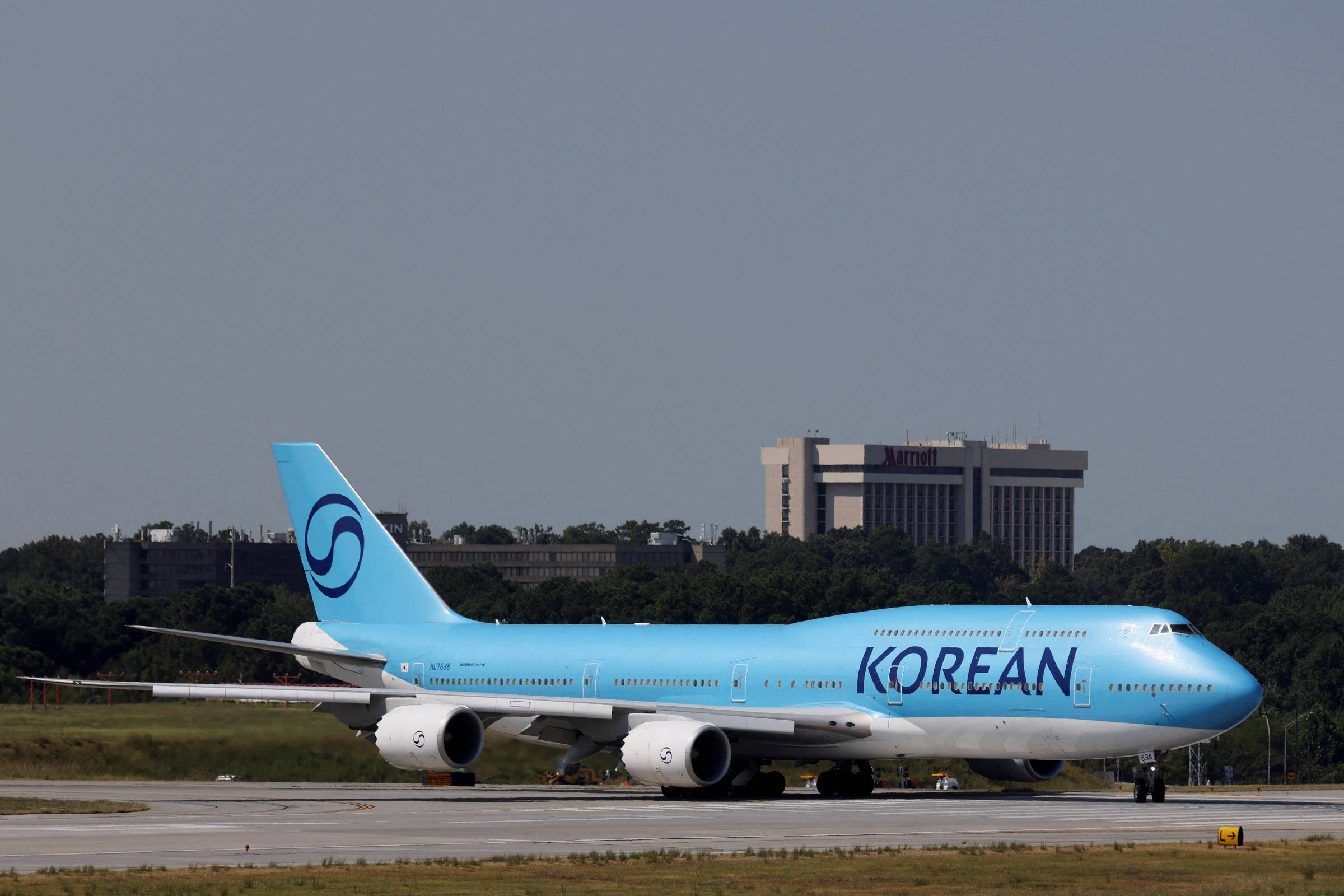 Um avião da Korean Air, modelo Boeing 747, está taxiando na pista de um aeroporto. A aeronave é predominantemente azul, com a palavra