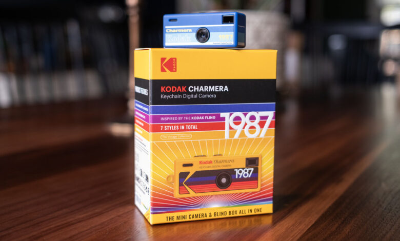 A blue Kodak Charmera keychain digital camera is placed on top of its colorful yellow and red box, which features bold