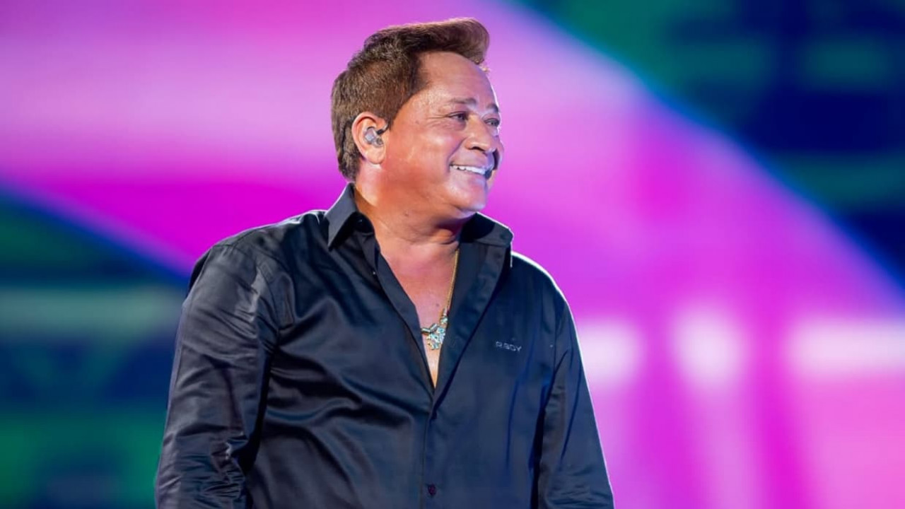 Leonardo no palco, de camisa social preta, olhando para o lado e sorrindo